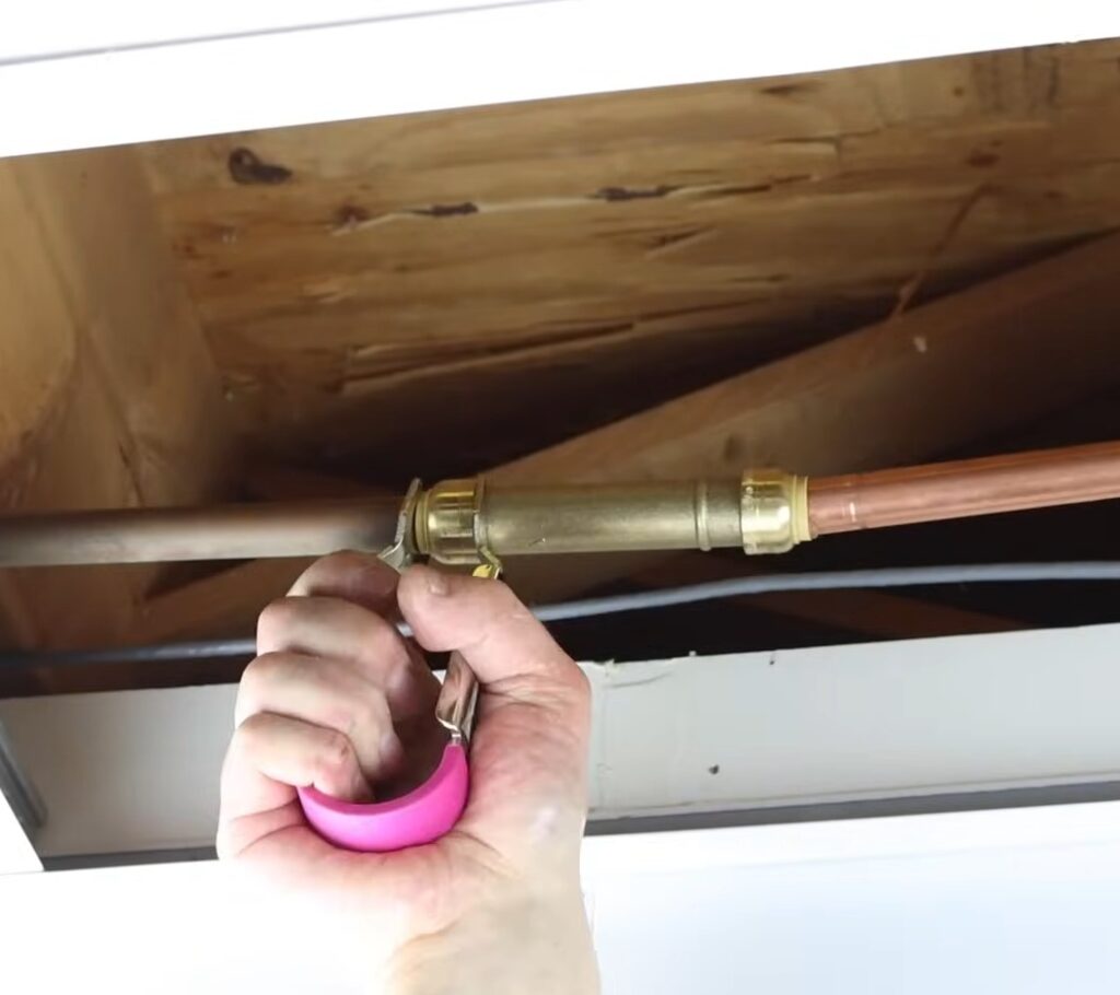 Plumber repairing a copper pipe under a floor