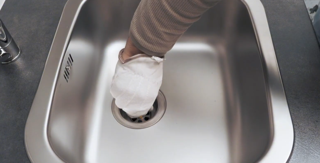 Person wearing gloves cleaning sink drain
